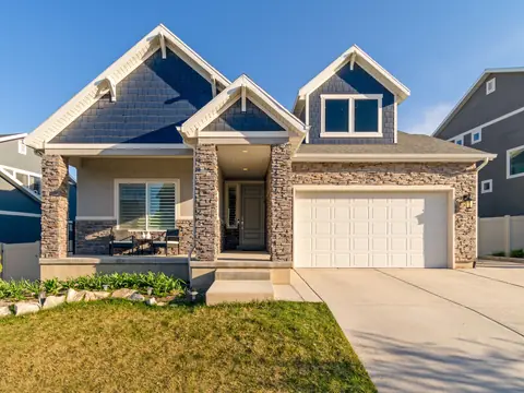 A two-story suburban home with blue shake siding, a stacked-stone front porch and a white double garage door under a clear blue sky